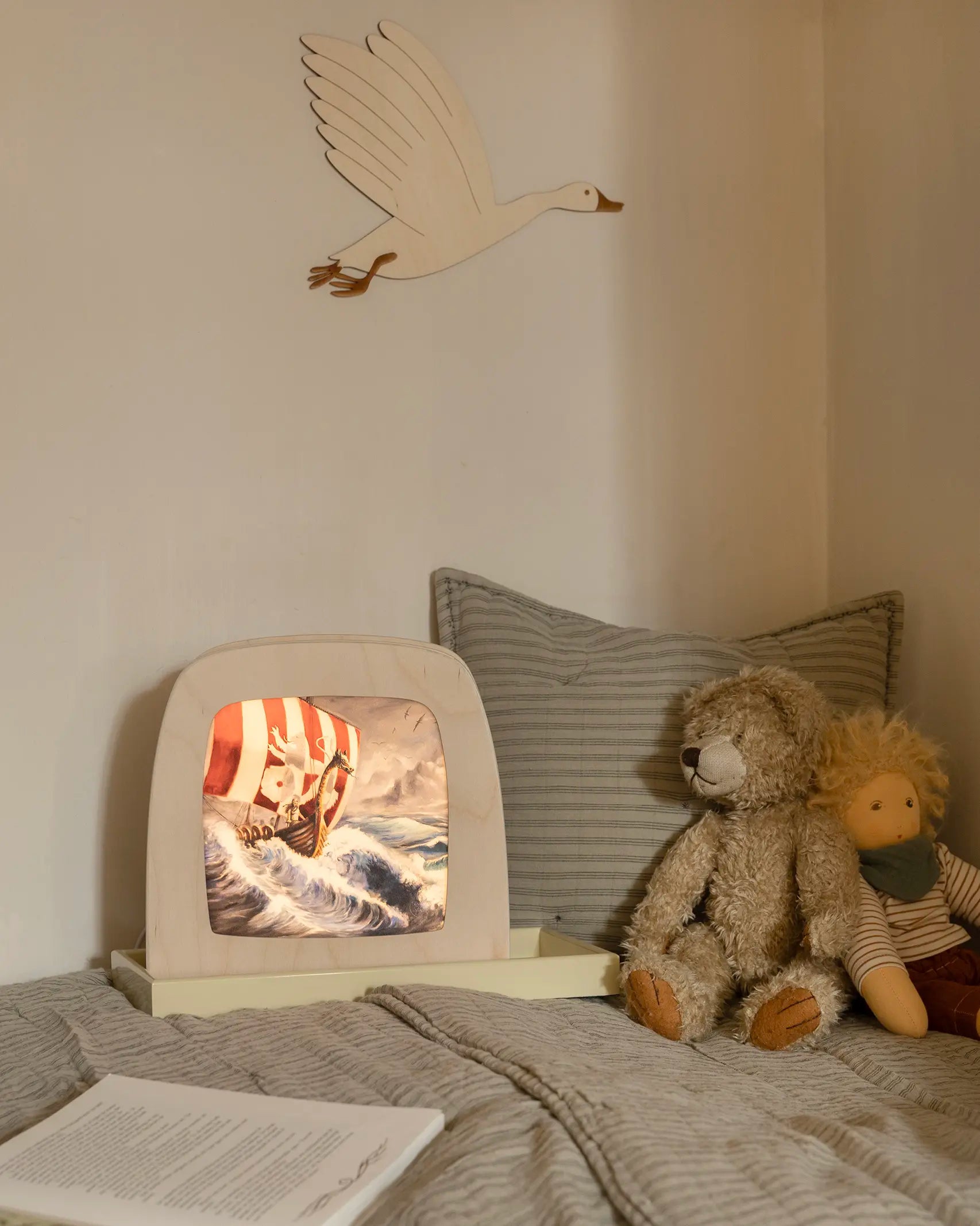 Toverlux Magic Lamp with artwork by Berit Strasser showing a Viking Ship sailing through the sea, on a child's bed next to a teddy bear and Nanchen Waldorf doll.