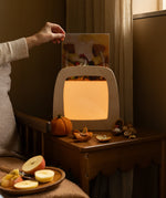 Hand holding an autumn silhouette for the Toverlux Magic Lamp by Het Wol Feetje in bedroom setting.