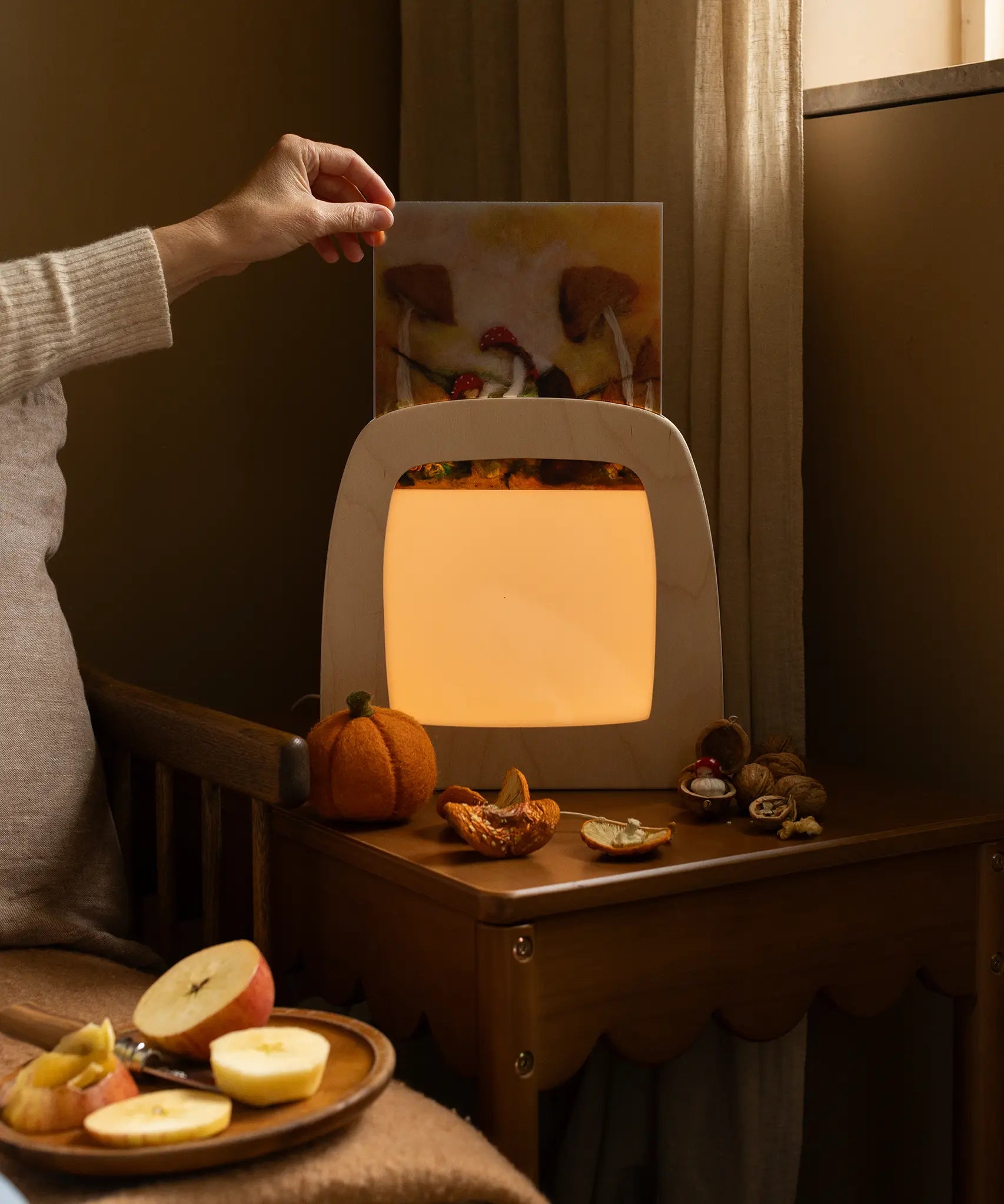 Hand holding an autumn silhouette for the Toverlux Magic Lamp by Het Wol Feetje in bedroom setting.