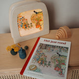 A cosy display with the Toverlux August silhouette in a wooden lantern by Elsa Beskow standing on a wooden surface next to a Grimms rainbow and Grapat cup available at Babipur.