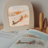 A cosy setup with the Toverlux February silhouette in a wooden lantern by Elsa Beskow standing on top of matching year book. Silhouette available at Babipur.
