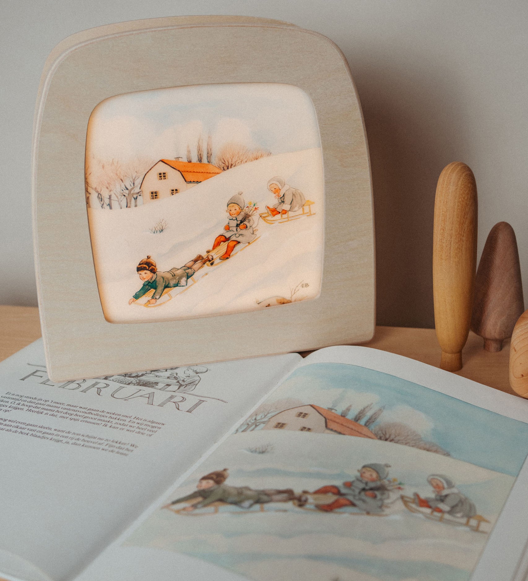 A cosy setup with the Toverlux February silhouette in a wooden lantern by Elsa Beskow standing on top of matching year book. Silhouette available at Babipur.