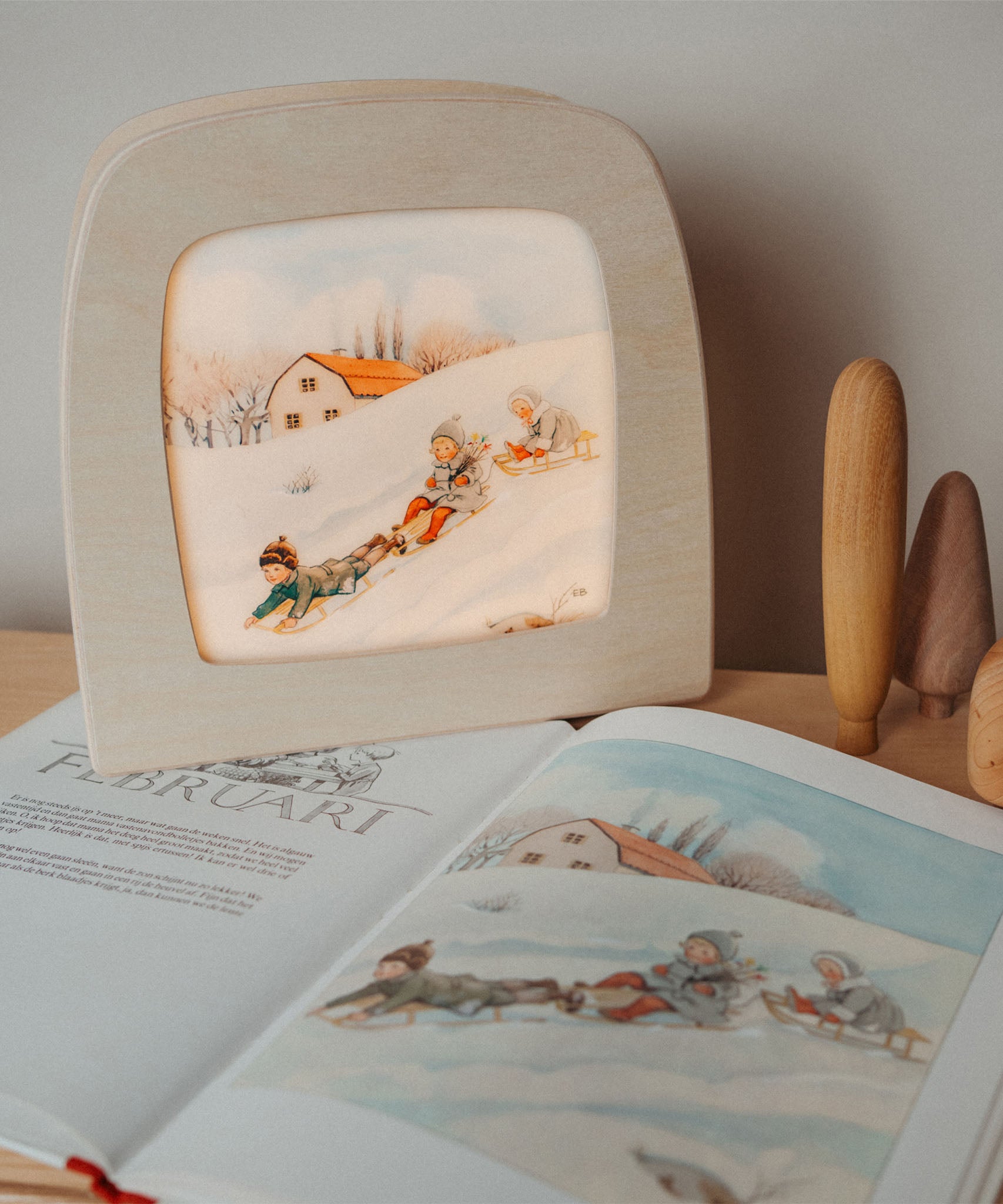 A cosy setup with the Toverlux February silhouette in a wooden lantern by Elsa Beskow standing on top of matching year book. Silhouette available at Babipur.