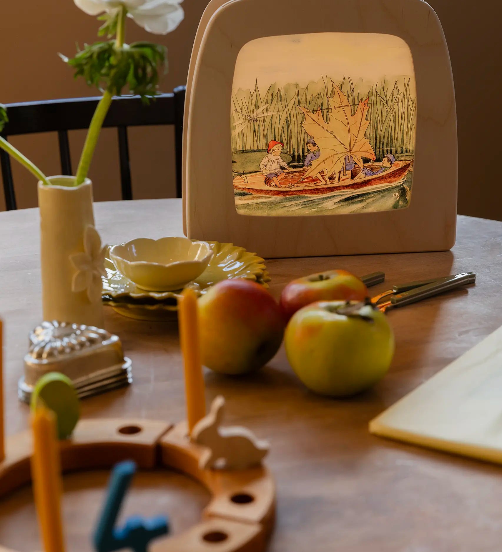 Toverlux Magic Lamp on table displaying artwork by Elsa Beskow, Peter in blueberry land, kids on a boat with a leaf sail.