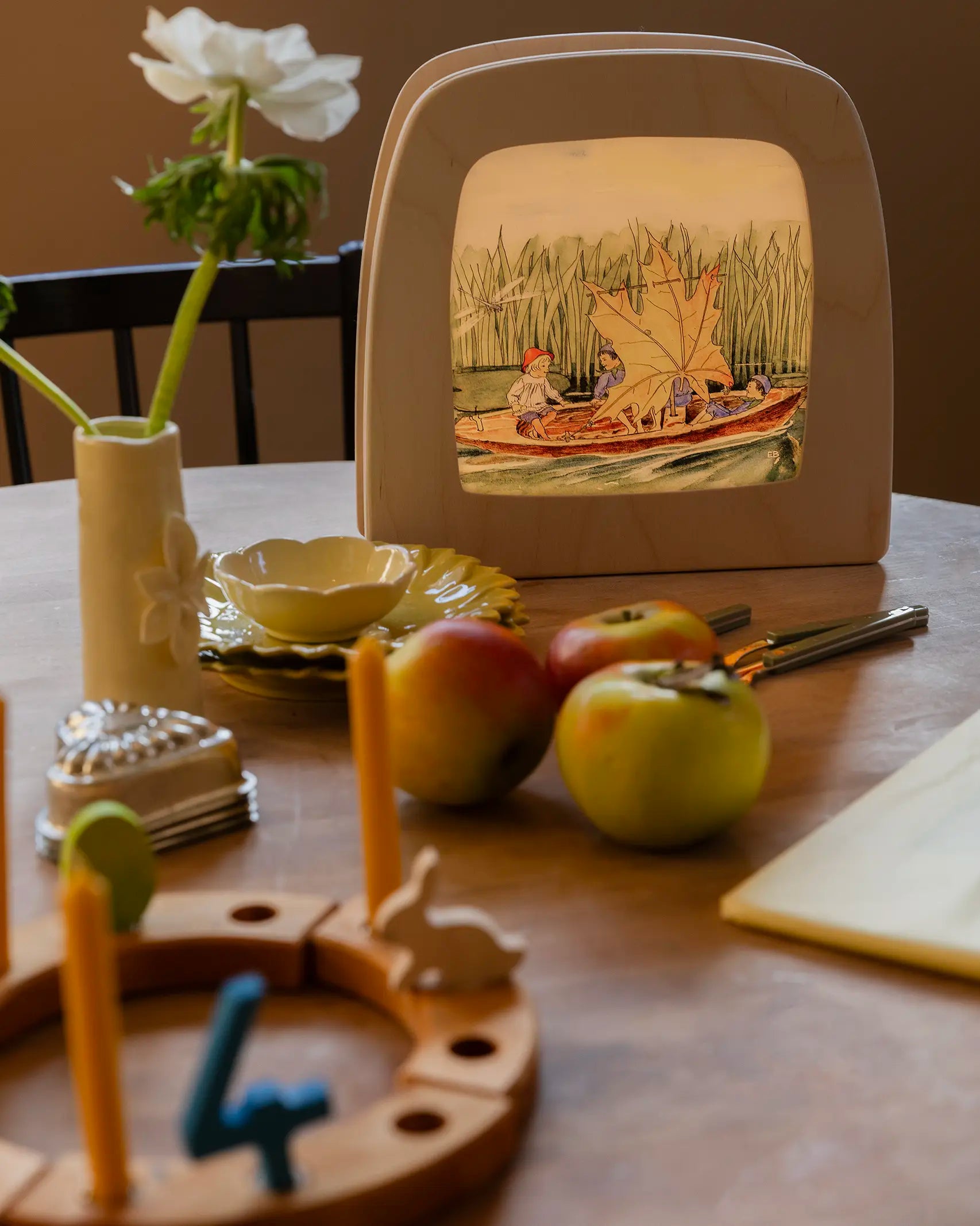 Toverlux Magic Lamp on table displaying artwork by Elsa Beskow, Peter in blueberry land, kids on a boat with a leaf sail.