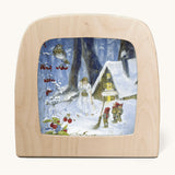 A Toverlux silhouette from artist Daniella Drescher, compatible with the Magic Lamp or Magic Frame both available at Babipur. Silhouette is showing a illustration of a winter woodland scene with gnomes standing next to a cabin with a woman dressed in white