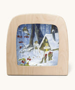 A Toverlux silhouette from artist Daniella Drescher, compatible with the Magic Lamp or Magic Frame both available at Babipur. Silhouette is showing a illustration of a winter woodland scene with gnomes standing next to a cabin with a woman dressed in white