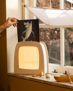 Hand placing a Toverlux Tijana Draws Whale silhouette into a Toverlux Magic Lamp Night Light Box on a windowsill.