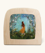 Toverlux Magic Lamp Silhouette - Artwork By Het Wol Feetje, Whispers Of Spring. An illustration of a felt person walking in a woodland area with white and purple flowers surrounding them. The image is on a cream background
