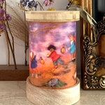 A beautiful illustration of Lantern Walk by Het Wol Feetje, inside a Toverlux Magic Lantern with flowers and a bronze coloured picture frame in the background