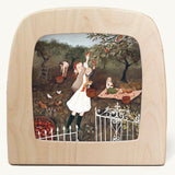 Orchard morning Toverlux Magic Lamp silhouette inside a wooden magic lamp. Artwork By Robin-Pieterse. A delicate painting style illustration of a woman and a child picking apples from a tree with a girl and a dog on a blanket in the background. This silhouette is available at Babipur