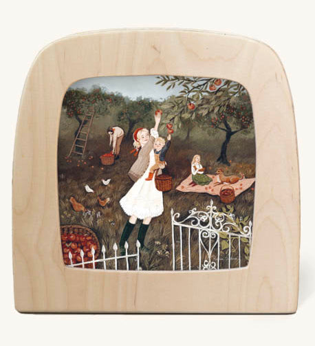 Orchard morning Toverlux Magic Lamp silhouette inside a wooden magic lamp. Artwork By Robin-Pieterse. A delicate painting style illustration of a woman and a child picking apples from a tree with a girl and a dog on a blanket in the background. This silhouette is available at Babipur