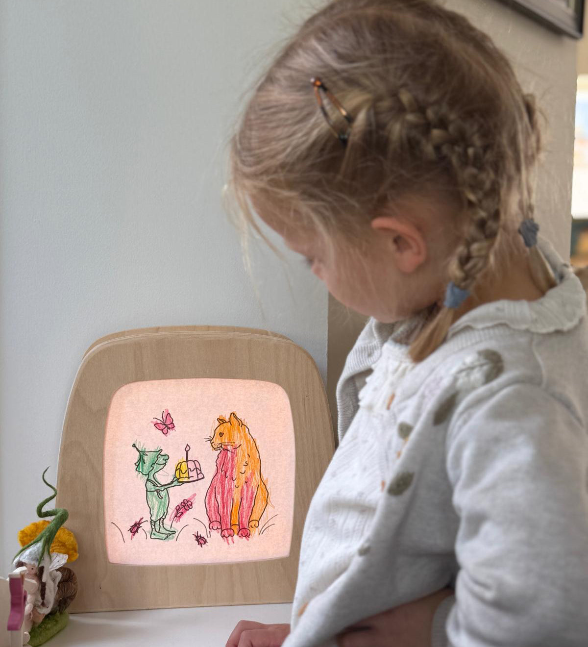 A child standing next to a Toverlux light frame with a silhouette of a cat and goblin from the story colouring book