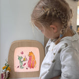 A child standing next to a Toverlux light frame with a silhouette of a cat and goblin from the story colouring book