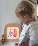 A child standing next to a Toverlux light frame with a silhouette of a cat and goblin from the story colouring book