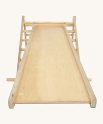 Triclimb wooden Miri slide attached to a natural Triclimb wooden pikler climbing frame showing the smooth side of the slide that can be used as a ramp or slide.