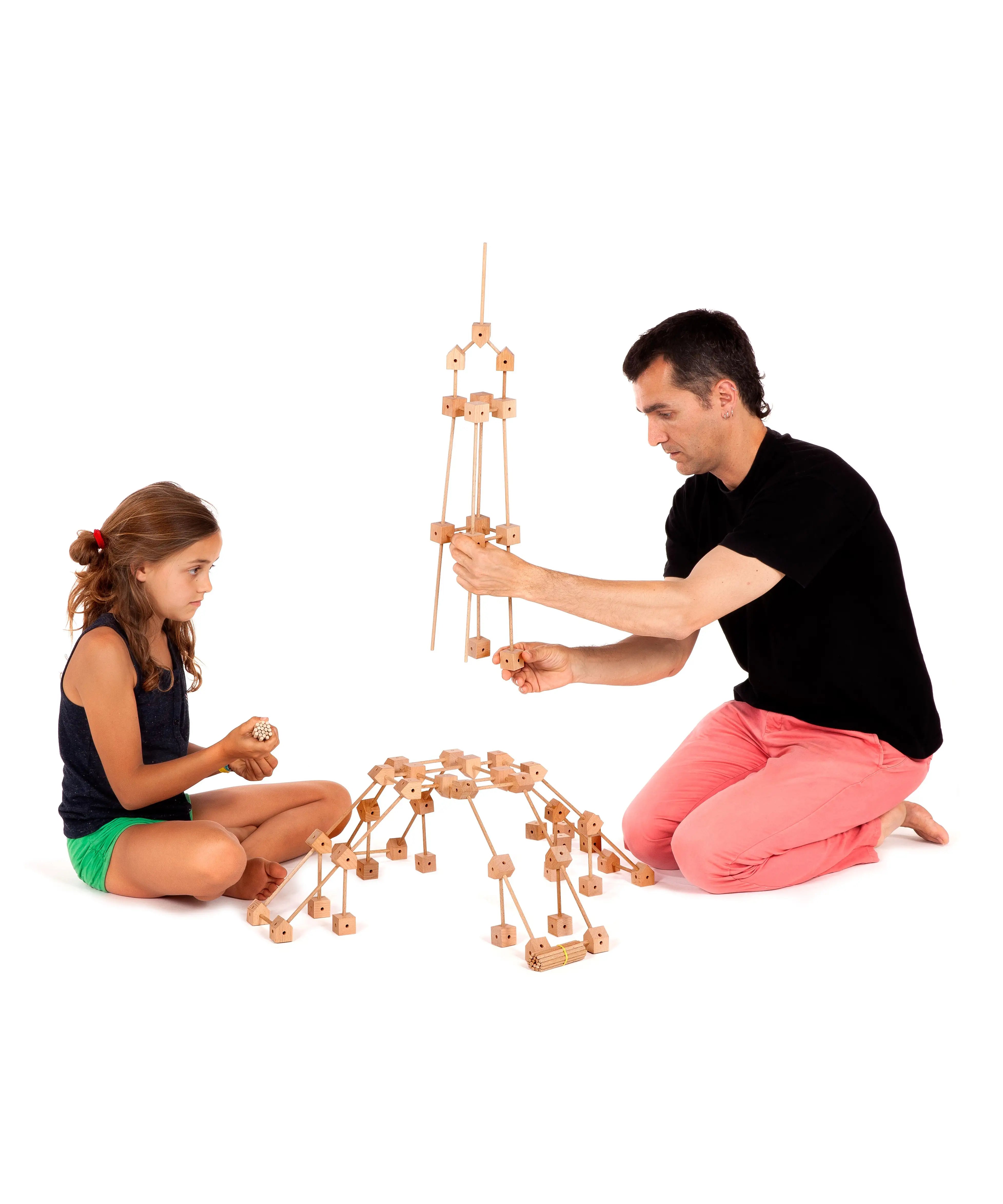 Father and daughter building a tower A using various wooden poles and blocks from the Trigonos mini large construction set