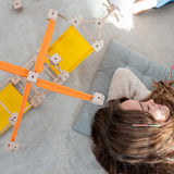 A helicopter made from the wooden poles, blocks and orange and yellow cotton sheets standing next to a sleeping child
