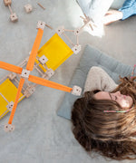 A helicopter made from the wooden poles, blocks and orange and yellow cotton sheets standing next to a sleeping child