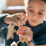 Child assembling various wooden poles and blocks out of the Trigonos mini large construction set 