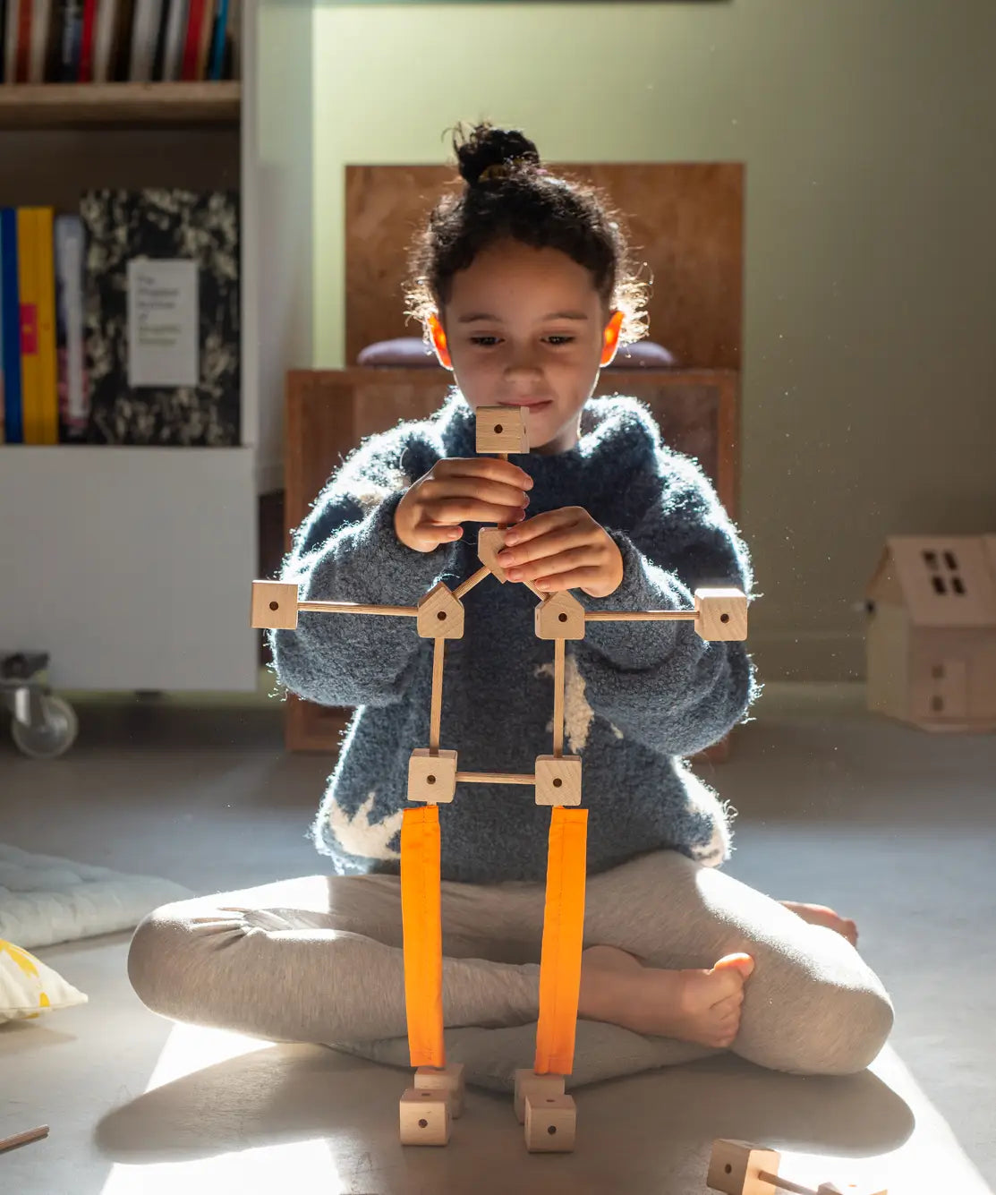 A child building  a robot various wooden poles and blocks and orange sheets  from the Trigonos mini large construction set