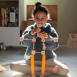 A child building  a robot various wooden poles and blocks and orange sheets  from the Trigonos mini large construction set
