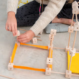 A child building a structure made from various wooden poles and blocks out of the Trigonos mini large construction set 