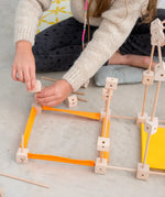 A child building a structure made from various wooden poles and blocks out of the Trigonos mini large construction set 