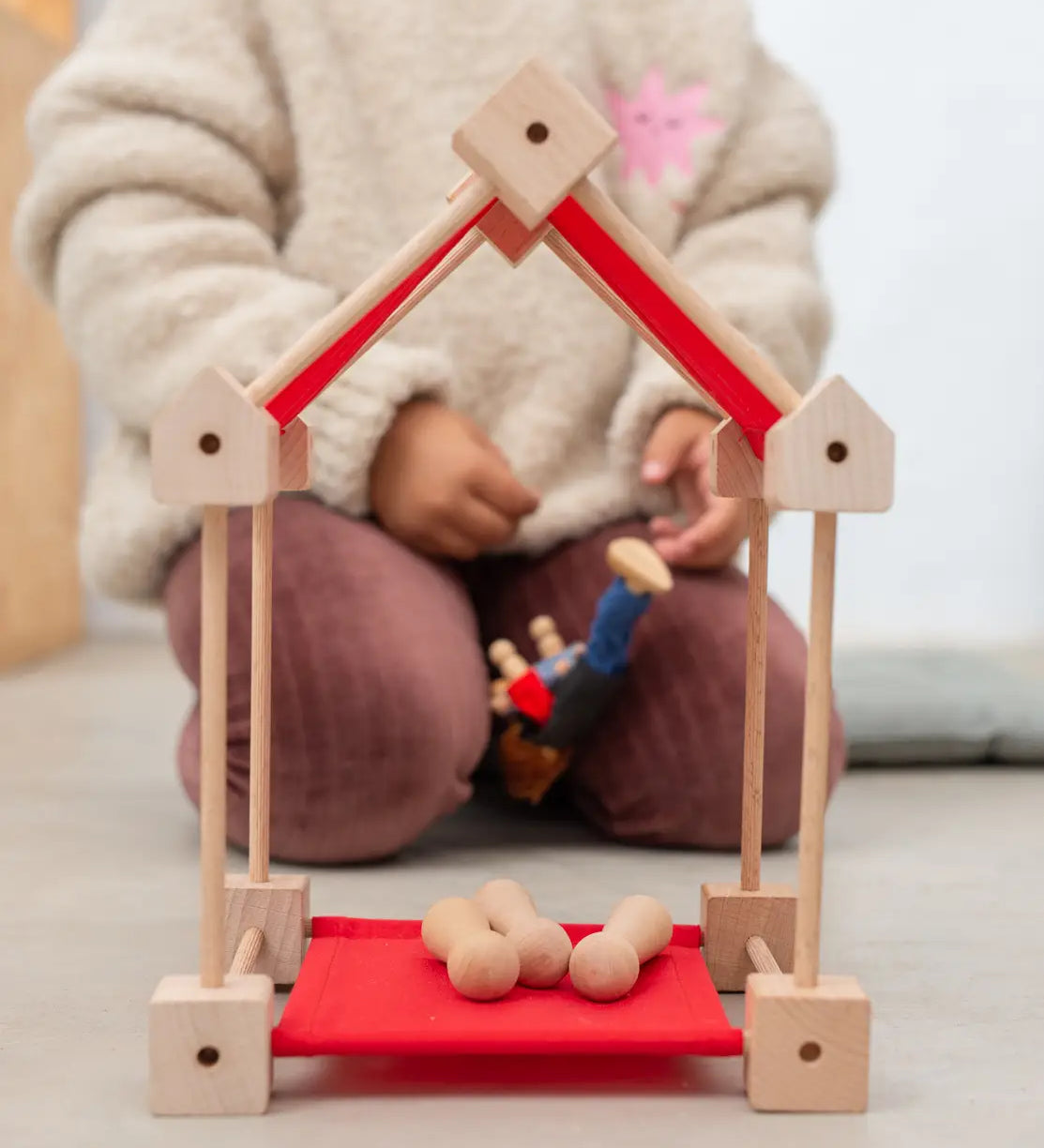 A simple house build from the Trigonos wooden mini construction kit with small balls inside on a red sheet