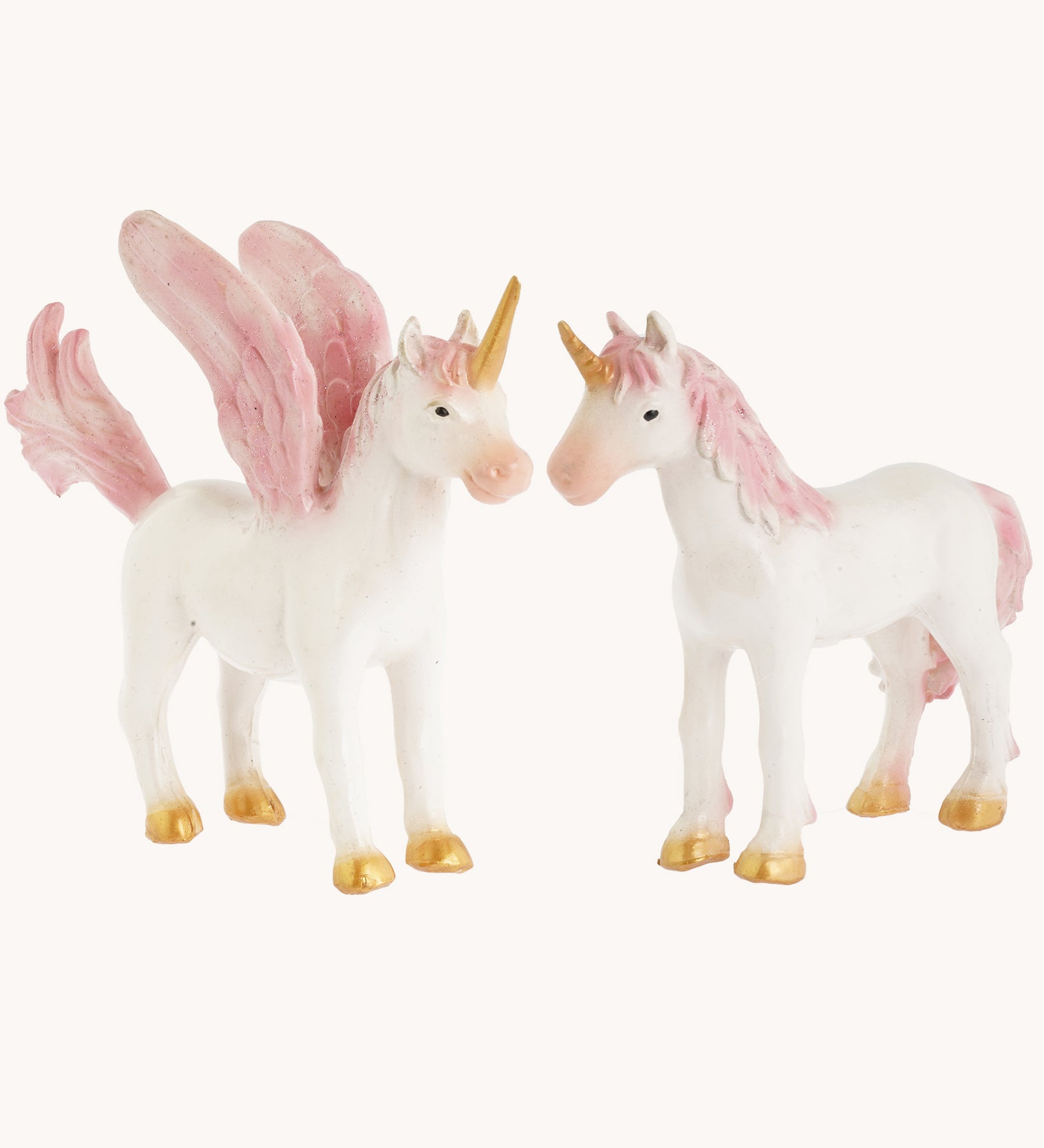 The Green Rubber Toys Rainbow Unicorn and Pegasus is a 2-pack of natural rubber, eco-friendly toy mythical horse figures with white bodies and pink details on the wings, tails and mane and golden hooves and horns. The image is on a cream background