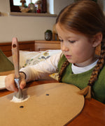 A little girl painting her VAH DIY wooden toy shield with white paint. 