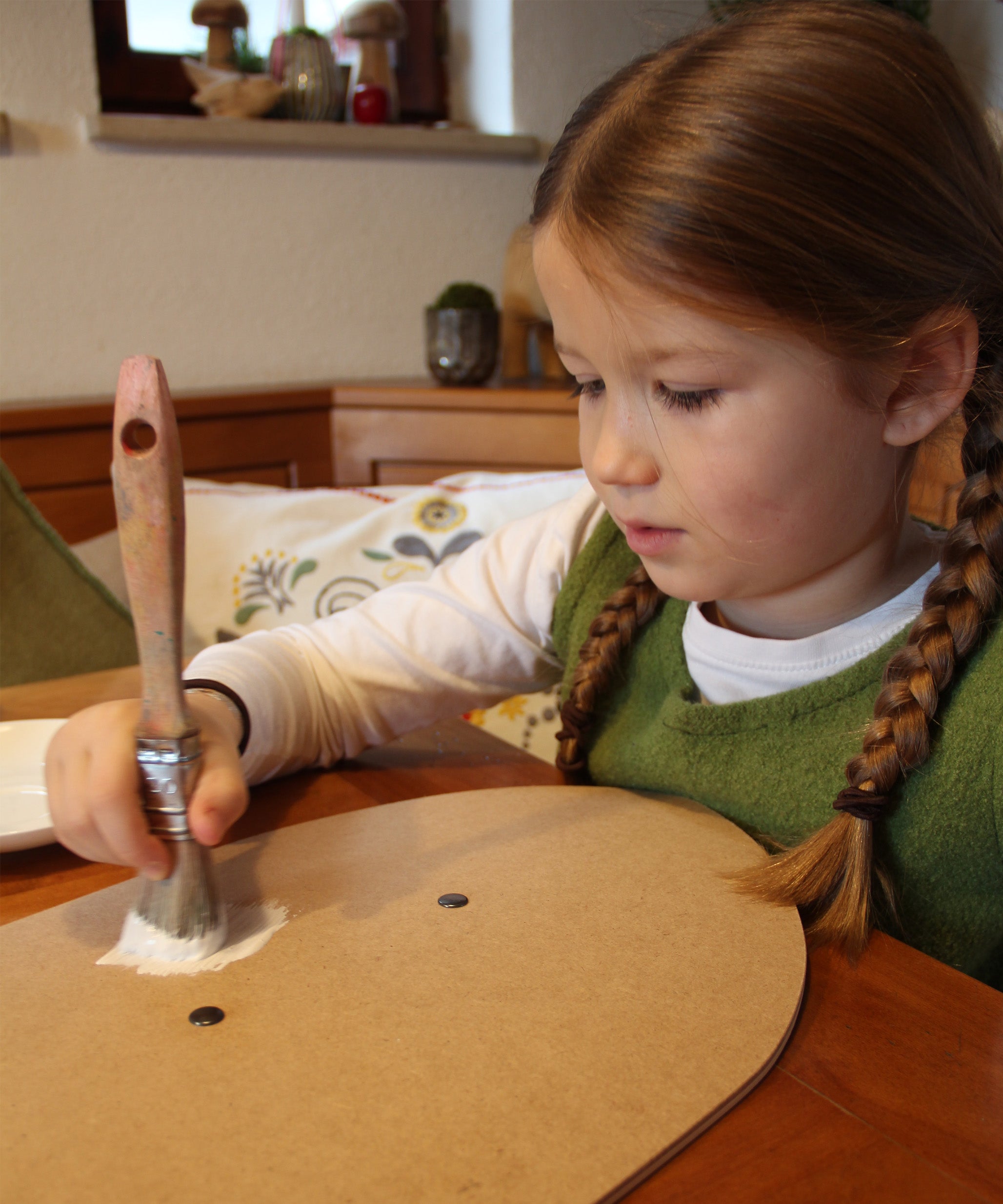 A little girl painting her VAH DIY wooden toy shield with white paint. 