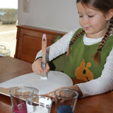 A little girl painting her VAH DIY wooden toy shield with white paint. 