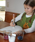 A little girl painting her VAH DIY wooden toy shield with white paint. 