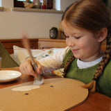 A little girl painting her VAH DIY wooden toy shield with white paint. 