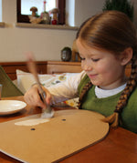 A little girl painting her VAH DIY wooden toy shield with white paint. 