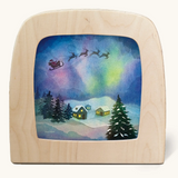 Toverlux silhouette of Father Christmas flying through the sky with Northern lights, snowy houses and Christmas trees, for December and Christmas Eve celebrations.