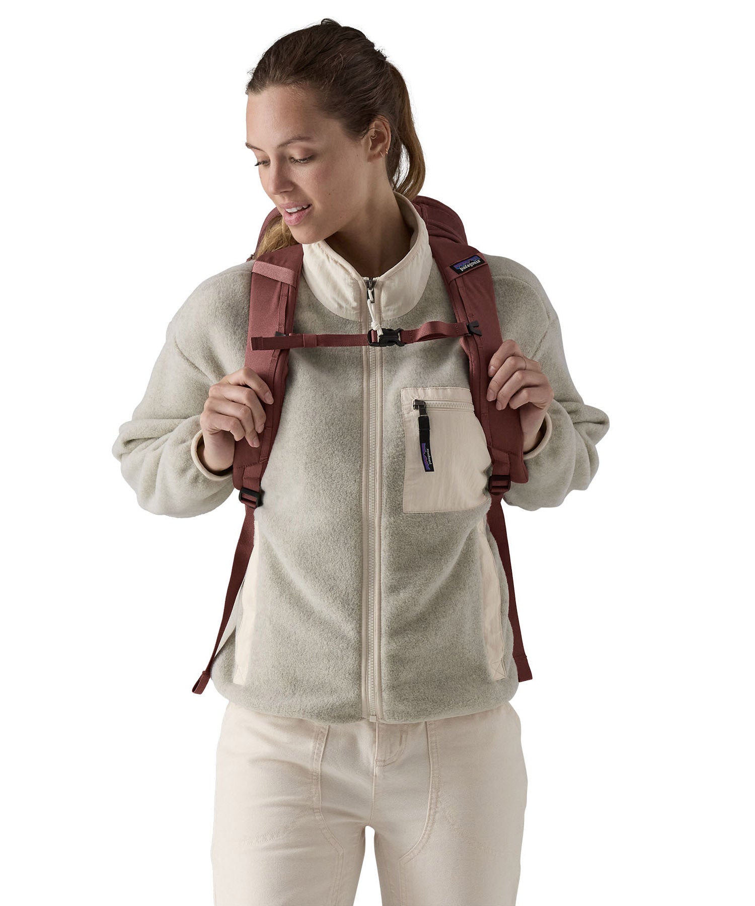 A view of the front of a woman wearing The Patagonia Black Hole Pack 32 litre capacity backpack in dulse mauve colour on her back.
