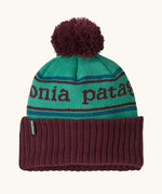 Patagonia Kids Powder Town Beanie in Park Stripe: Solo Teal. A teal knit with maroon 'Patagonia' woven around the head, a maroon rib-knit cuff, and a maroon pom-pom on top. 