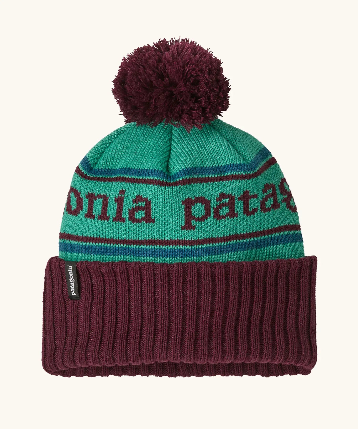 Patagonia Kids Powder Town Beanie in Park Stripe: Solo Teal. A teal knit with maroon 'Patagonia' woven around the head, a maroon rib-knit cuff, and a maroon pom-pom on top. 