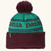 Patagonia Kids Powder Town Beanie in Park Stripe: Solo Teal. A teal knit with maroon 'Patagonia' woven around the head, a maroon rib-knit cuff, and a maroon pom-pom on top. 