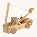The Walachia Wooden Catapult made from wooden pieces, on a cream background. The image shows the catapult with a small wooden ball inside the movable arm, with a string attached to the arm and to a vertical piece of wood in front.