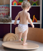 Wobbel 360, a wooden circle balance board toy for children with felt backing, being played with by child in a playroom.