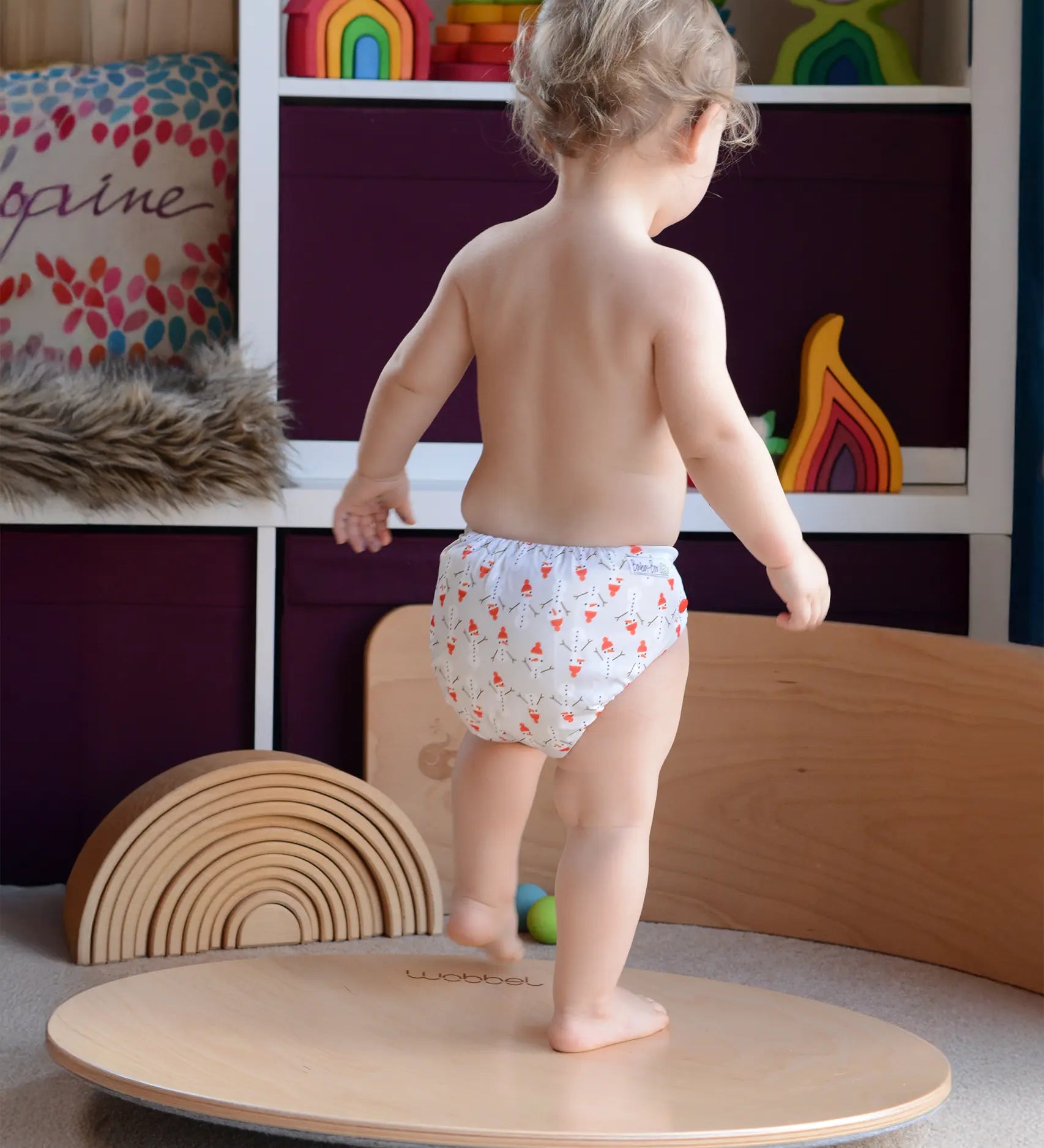 Wobbel 360, a wooden circle balance board toy for children with felt backing, being played with by child in a playroom.