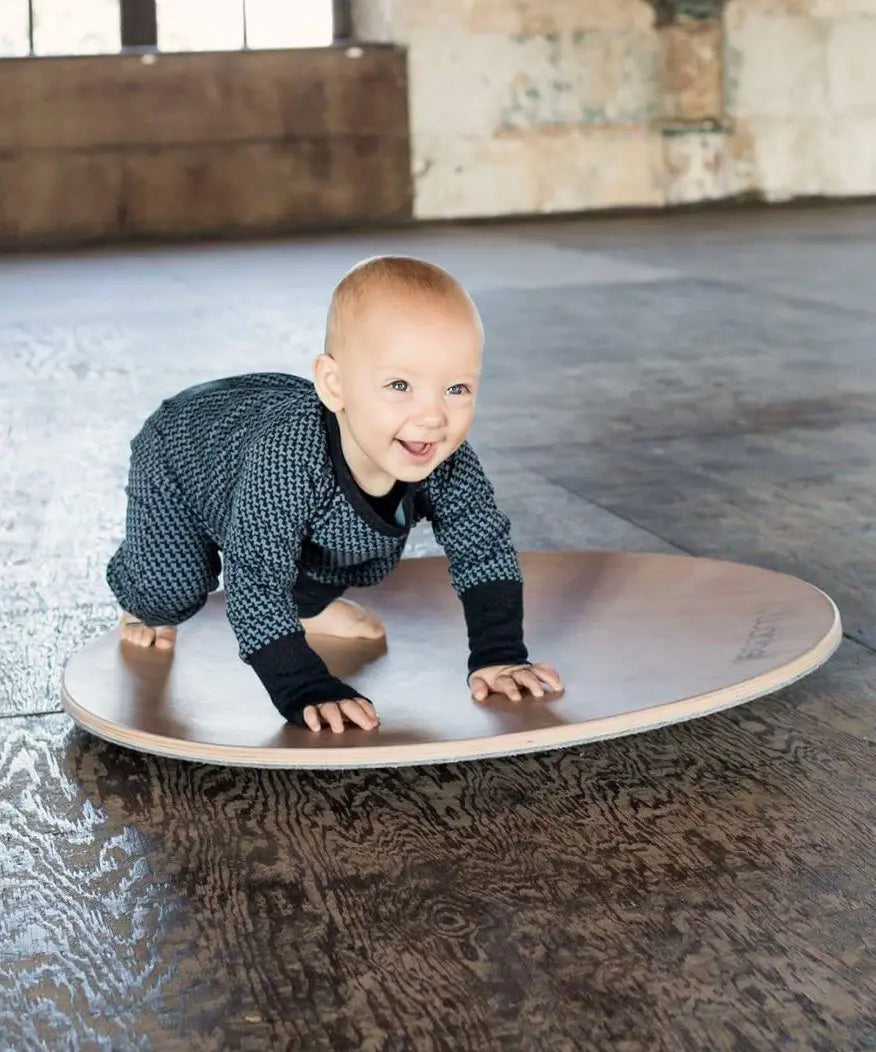 Wobbel 360, a wooden circular balance board toy, being played with by a baby.