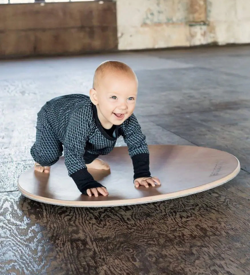 Wobbel 360, a wooden circular balance board toy, being played with by a baby.