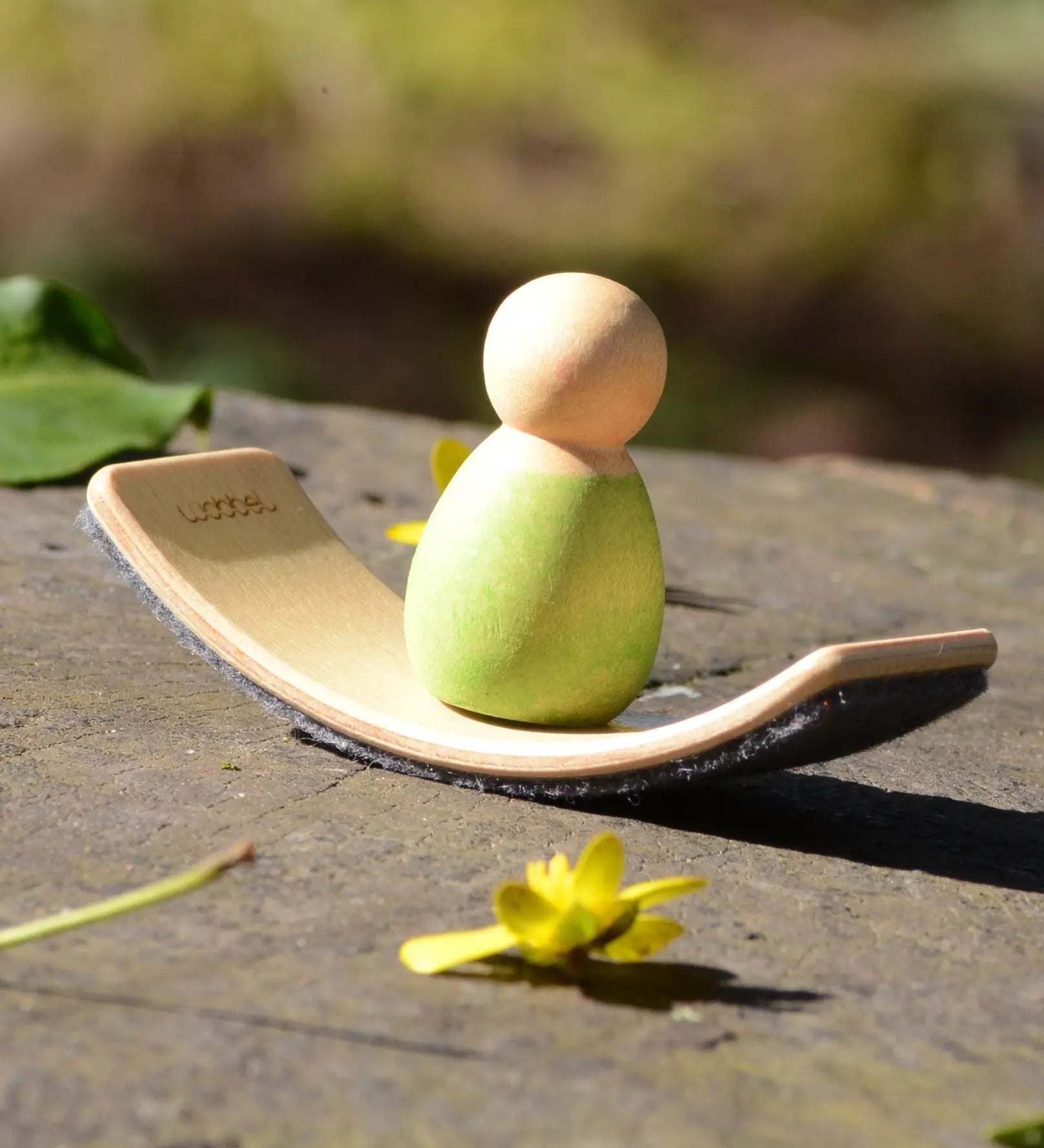 Mini Wooden Wobbel Balance Board for your peg dolls, a pocket-sized dollhouse size board, outside with a baby Nin on it.