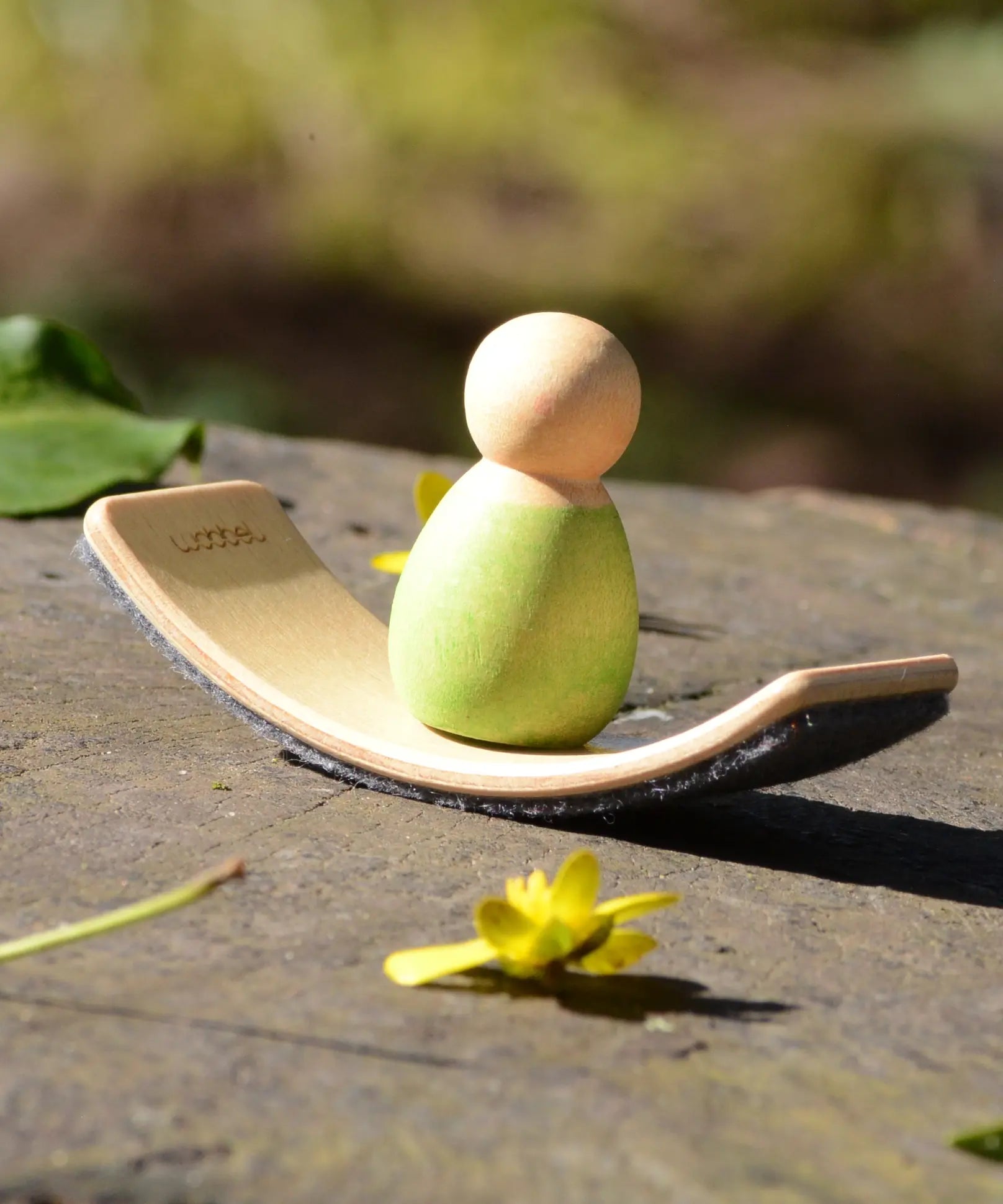 Mini Wooden Wobbel Balance Board for your peg dolls, a pocket-sized dollhouse size board, outside with a baby Nin on it.