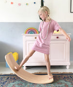 Wobbel original balance board, made from beech wood, being played with by young girl in a playroom.