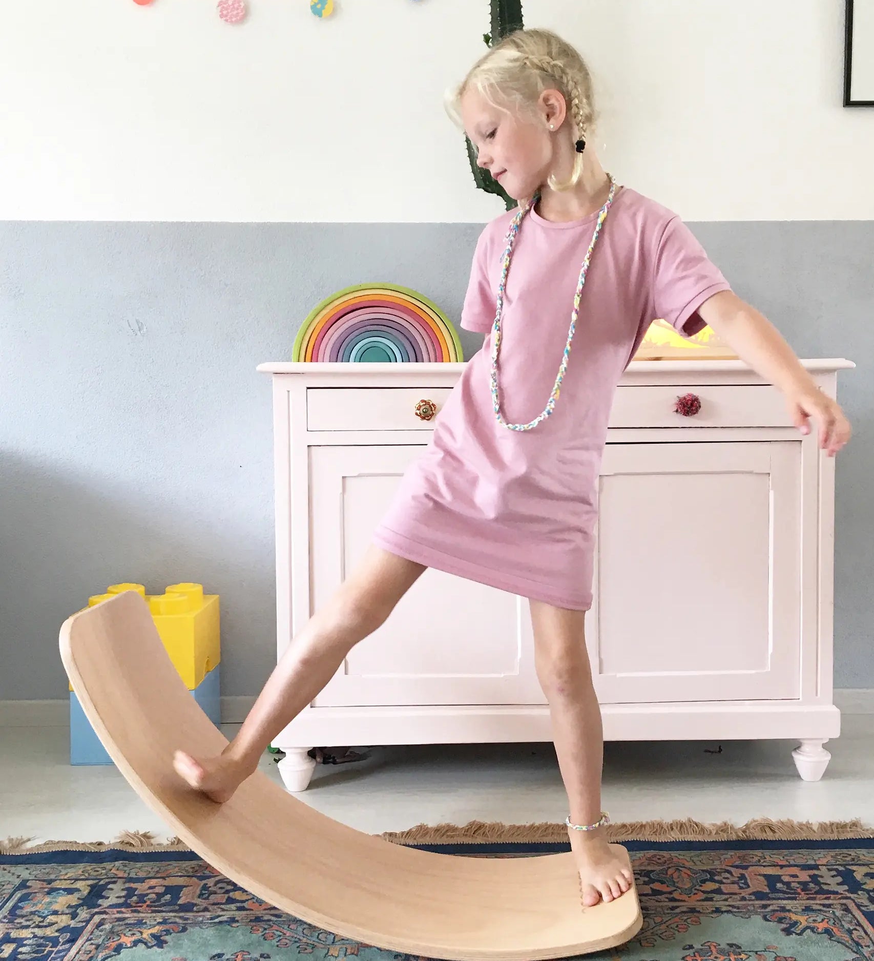 Wobbel original balance board, made from beech wood, being played with by young girl in a playroom.